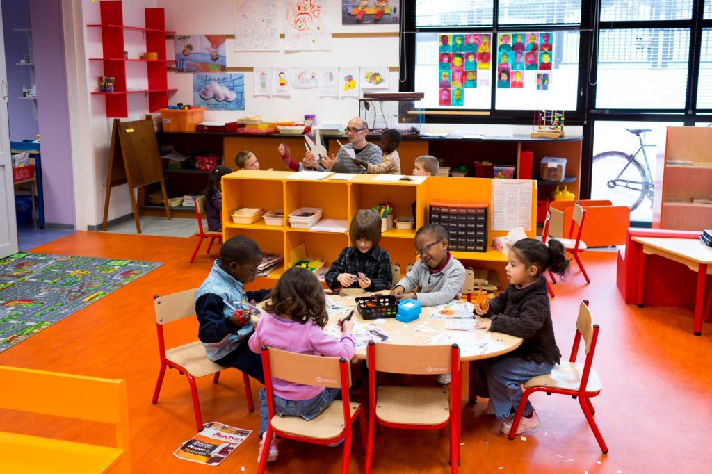 école maternelle, enfants assis autour d'une table en train de faire du collage